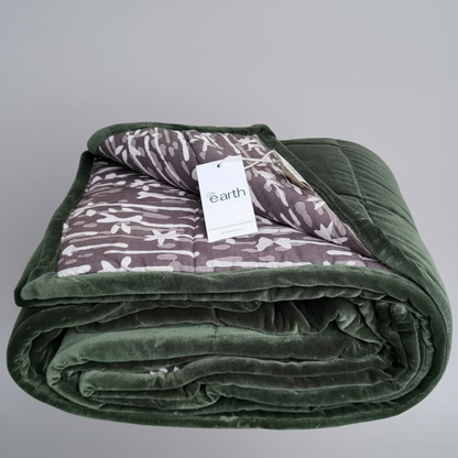 Eucalypt green velvet blanket with earth toned pattern on reverse cotton against a white wall.